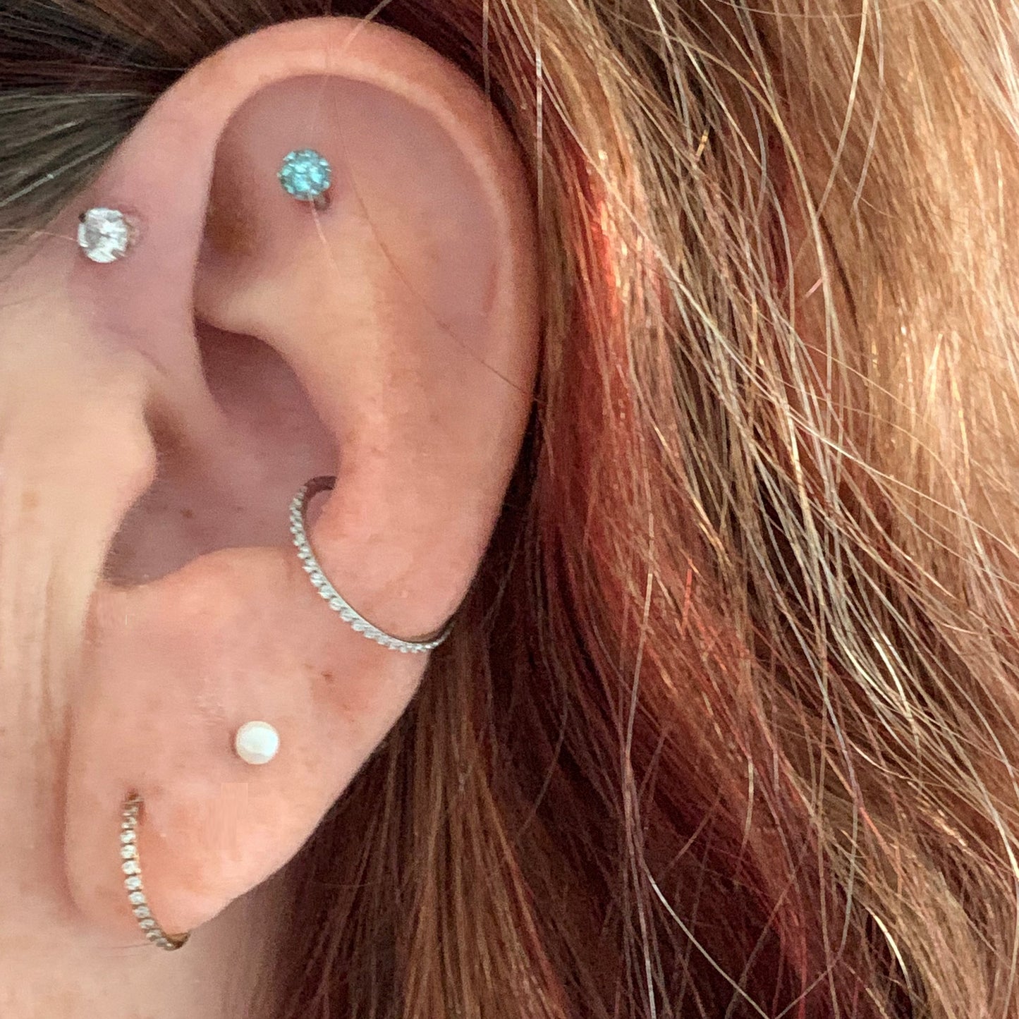 Side view of female model wearing the surgical steel segment ring with side facing gems in both the conch and ear lobe piercing.