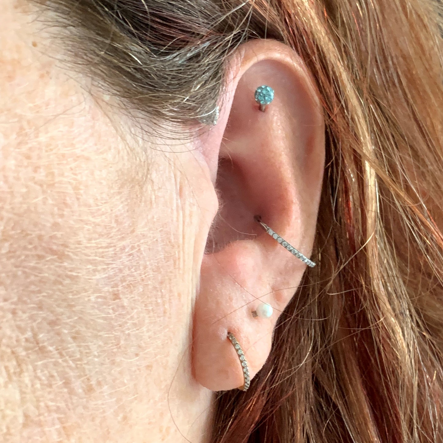 Side view of female model wearing the surgical steel segment ring with side facing gems in both the conch and ear lobe piercing.