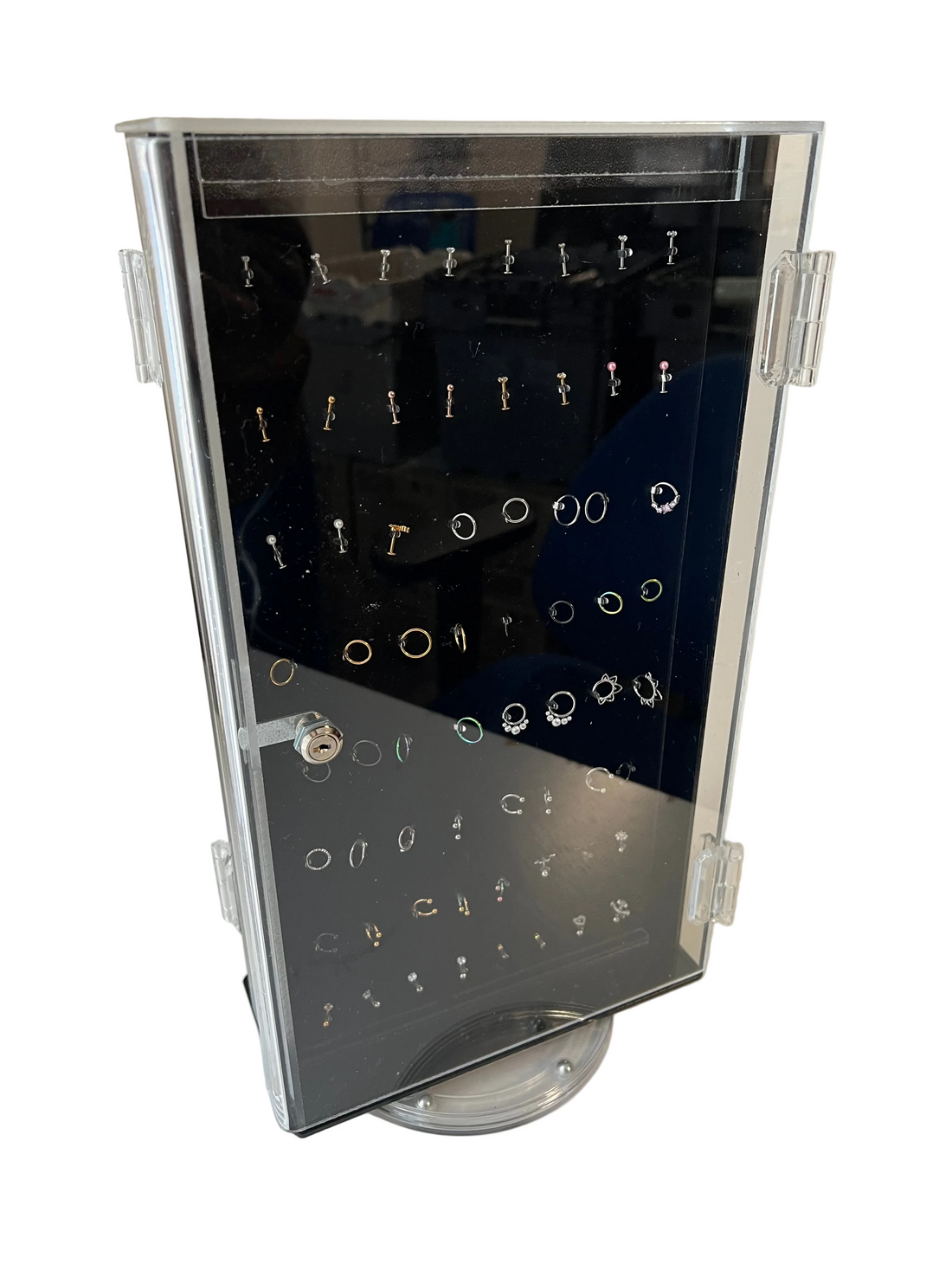 A 2-sided rotating clear acrylic countertop retail display case filled with rows of surgical steel body jewellery rings and studs, shown on a white background.