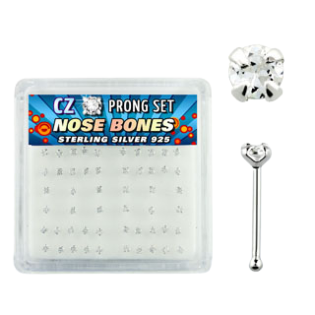 A clear acrylic display box filled with clear 2mm prong-set CZ nose bones. To the right, details show a close-up of a round clear gemstone and a straight nose bone post with a small ball end. The colourful label inside reads "CZ Prong Set Nose Bones Sterling Silver 925".