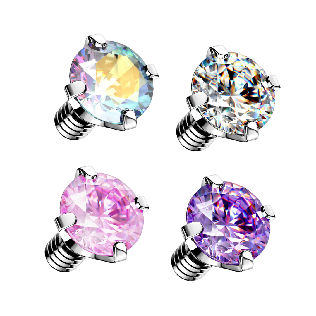 Four internally threaded surgical steel prong-set crystal piercing tops on a white background, featuring round brilliant-cut faceted gemstones in iridescent Aurora Borealis, clear white, light pink, and vibrant violet-purple colours.