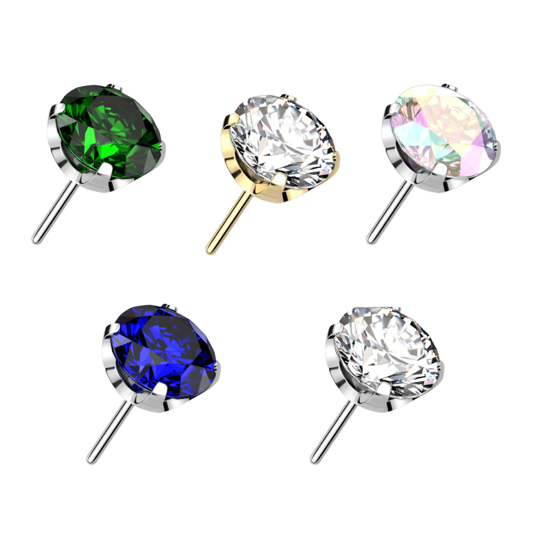 Five titanium threadless prong-set round gem piercing tops on a white background. Top row features a dark green crystal in a silver setting, a clear crystal in a gold-plated setting, and an iridescent aurora borealis crystal in a silver setting. Bottom row features a royal blue crystal and a clear crystal, both in silver settings.