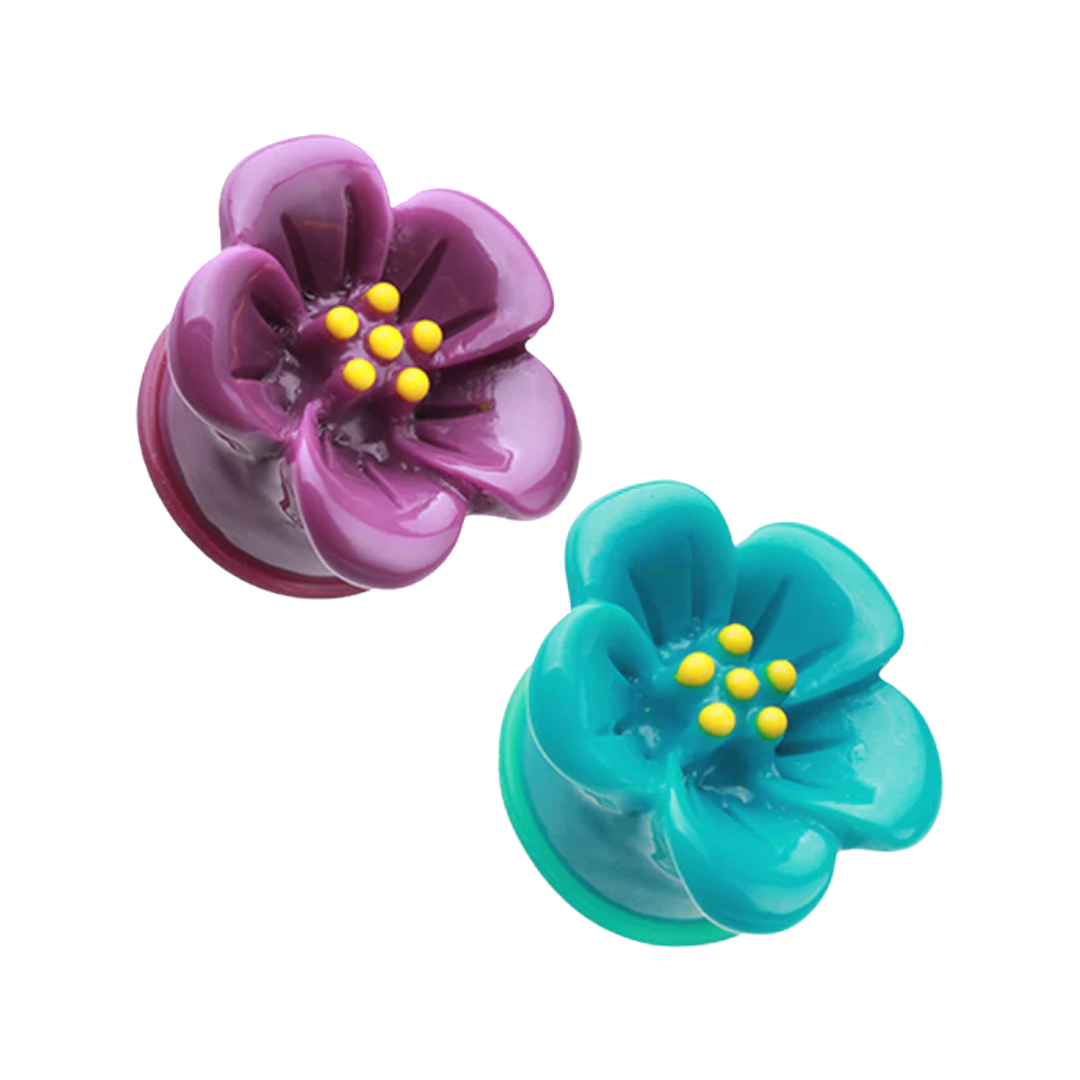 Two acrylic saddle plugs for stretched ear piercings featuring a three-dimensional carved hibiscus flower face with yellow stamen centers, with one plug in deep purple and the other in vibrant teal blue on a white background.