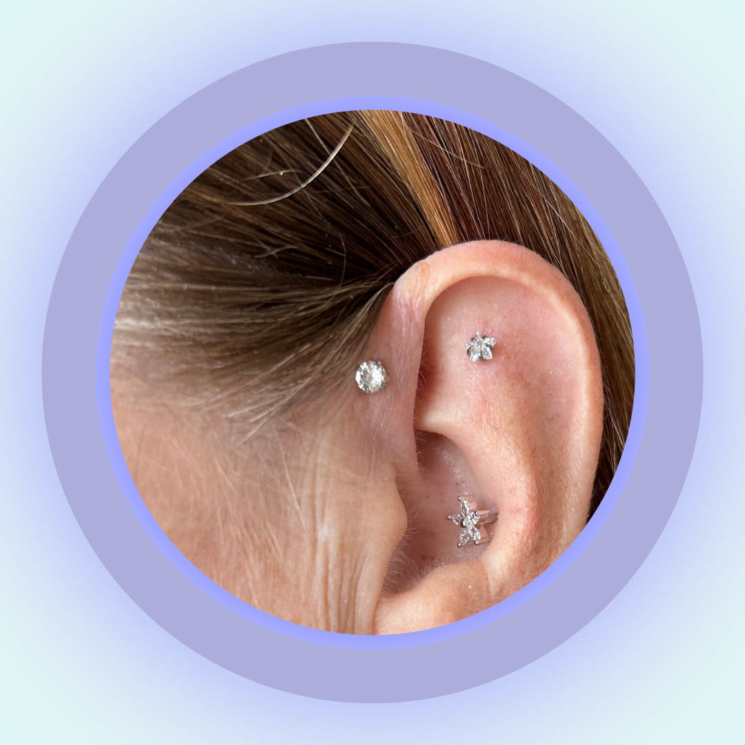 Close-up of an ear with multiple cubic zirconia stud earrings on a light purple background