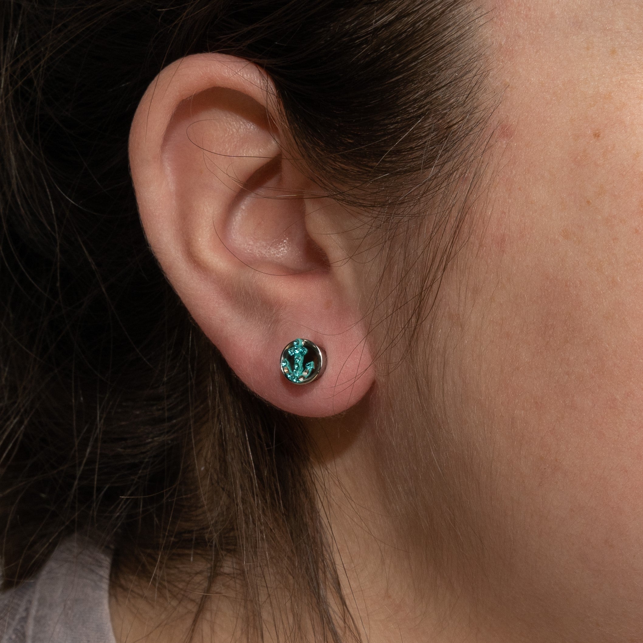 Silver round lobe earring with a sparkling turquoise anchor design.