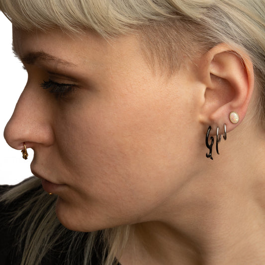 A model with various piercings is wearing a blackline devil horn stretcher in her lower lobe.