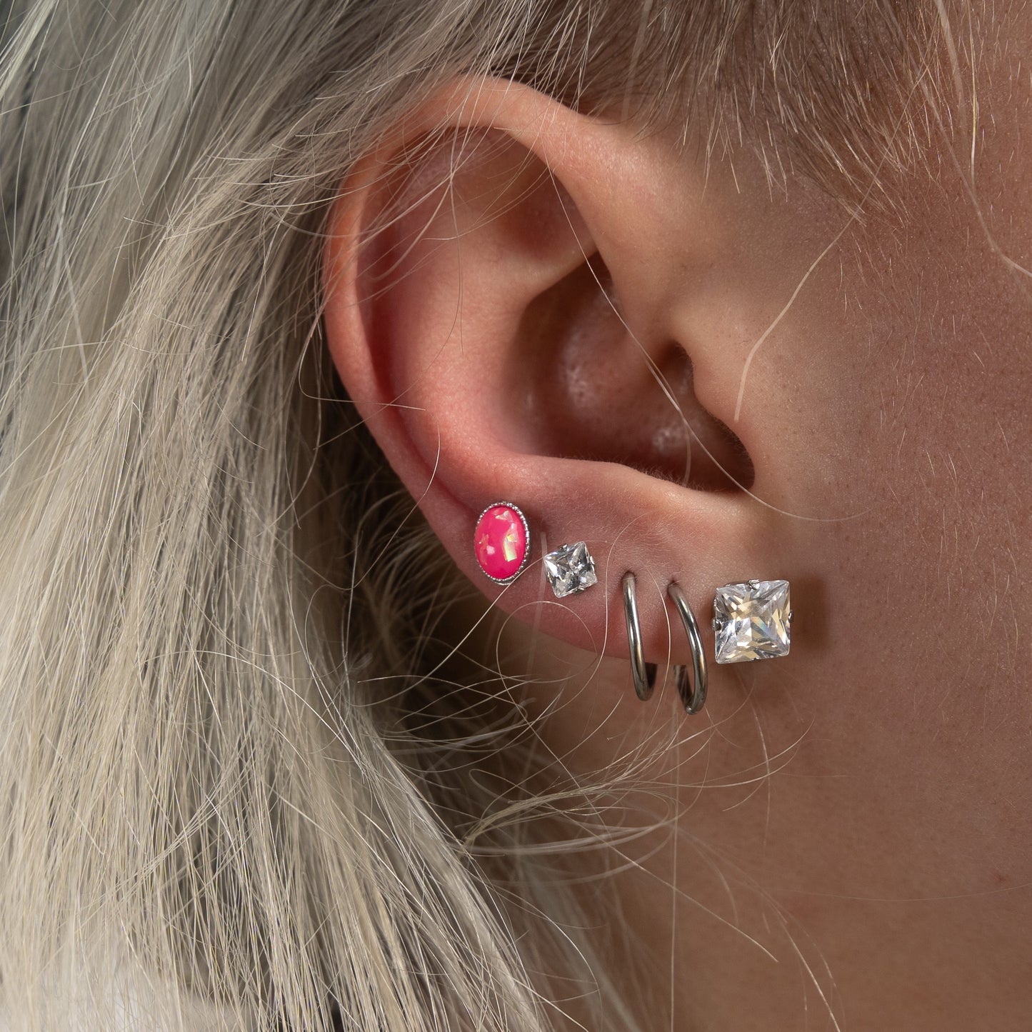 Model wearing the 316L surgical steel earrings that boast a stunning square, prong-set cubic zirconia, in two different lobe piercings, in different sizes.