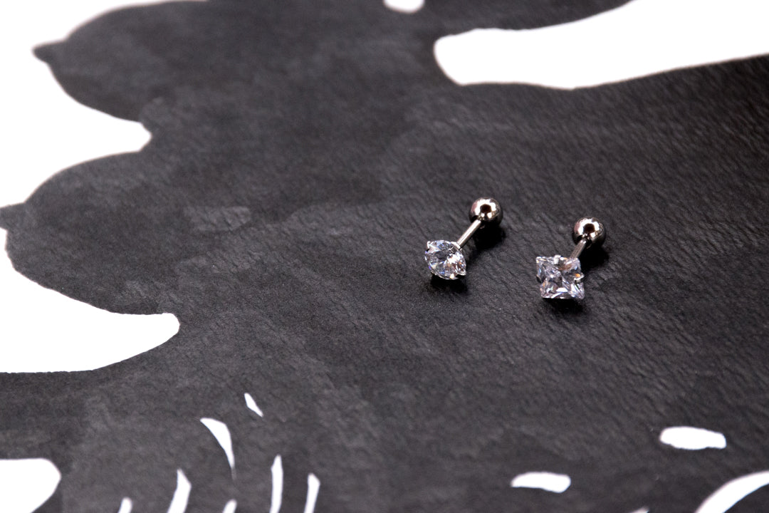 Two stainless steel cartilage barbells with prong-set clear CZ gems in round and square shapes.