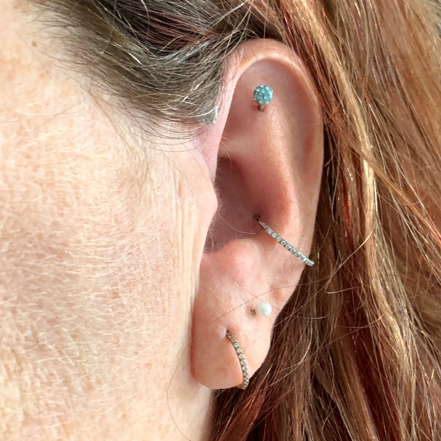 Side view of female model wearing the surgical steel segment ring with side facing gems  in both the conch and ear lobe piercing.