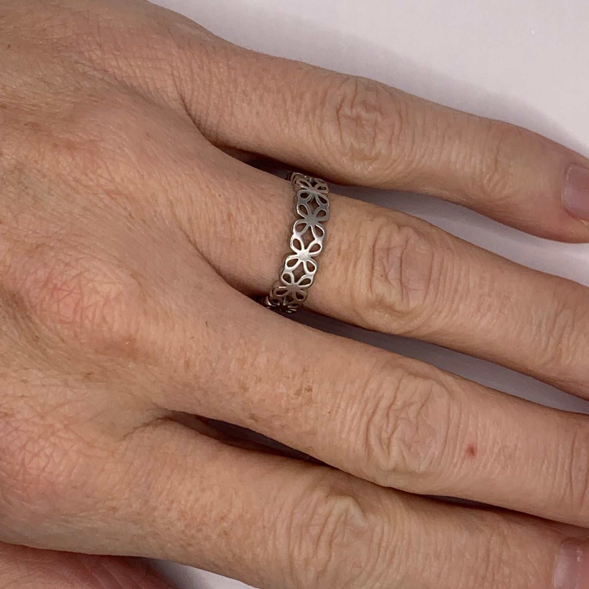 A hand wearing a stainless steel ring featuring a four-leaf or daisy flower cut-out design.