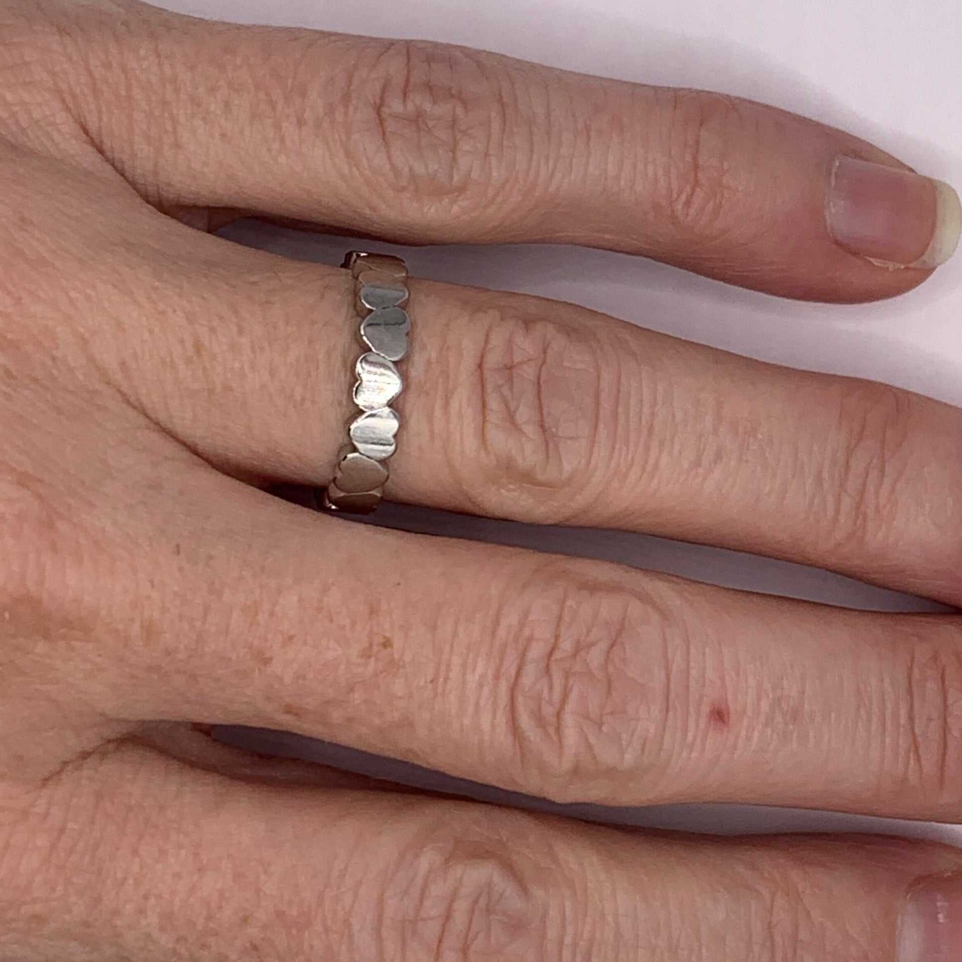 A stainless steel  ring featuring a continuous band of small heart shapes, styled as a stacking or promise ring