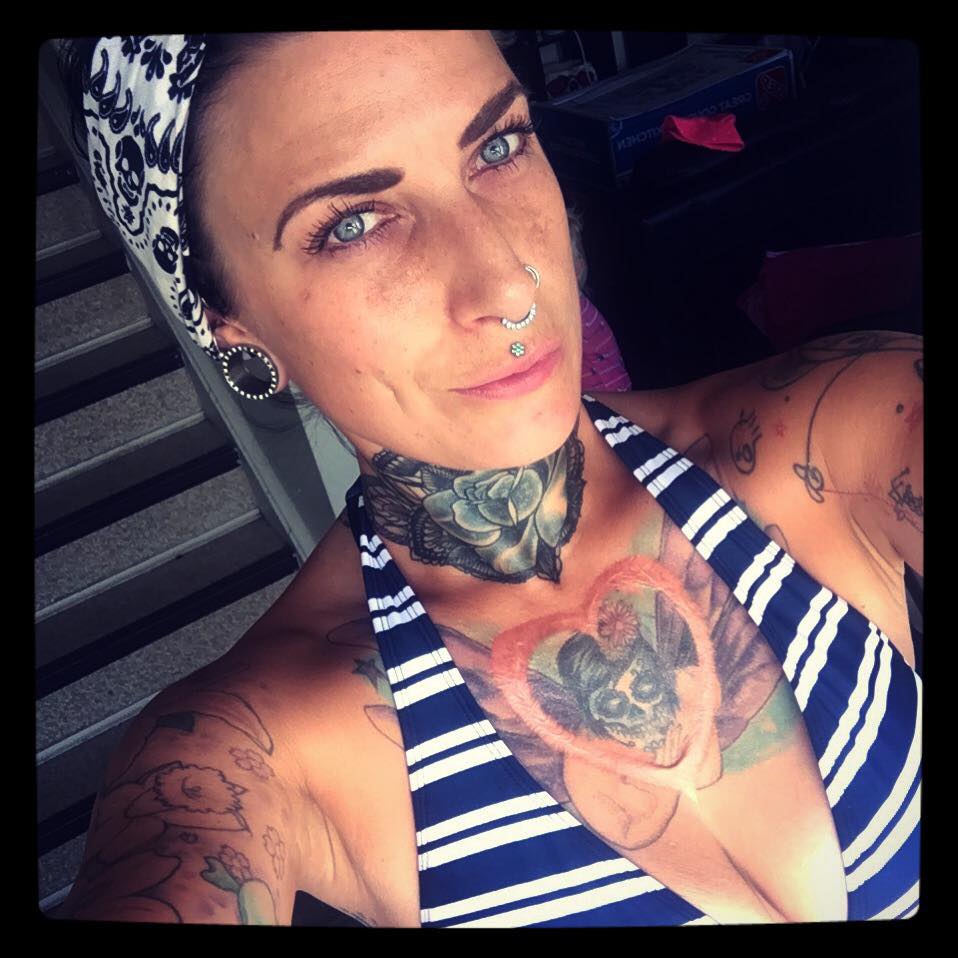 A portrait of a person with various tattoos, featuring a silver septum ring, a medusa piercing, and large black and white ear plugs.
